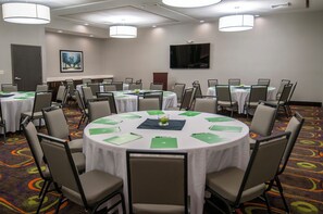 Une salle de conférence équipée de plusieurs tables, de chaises et d’un écran de télévision fixé au mur.