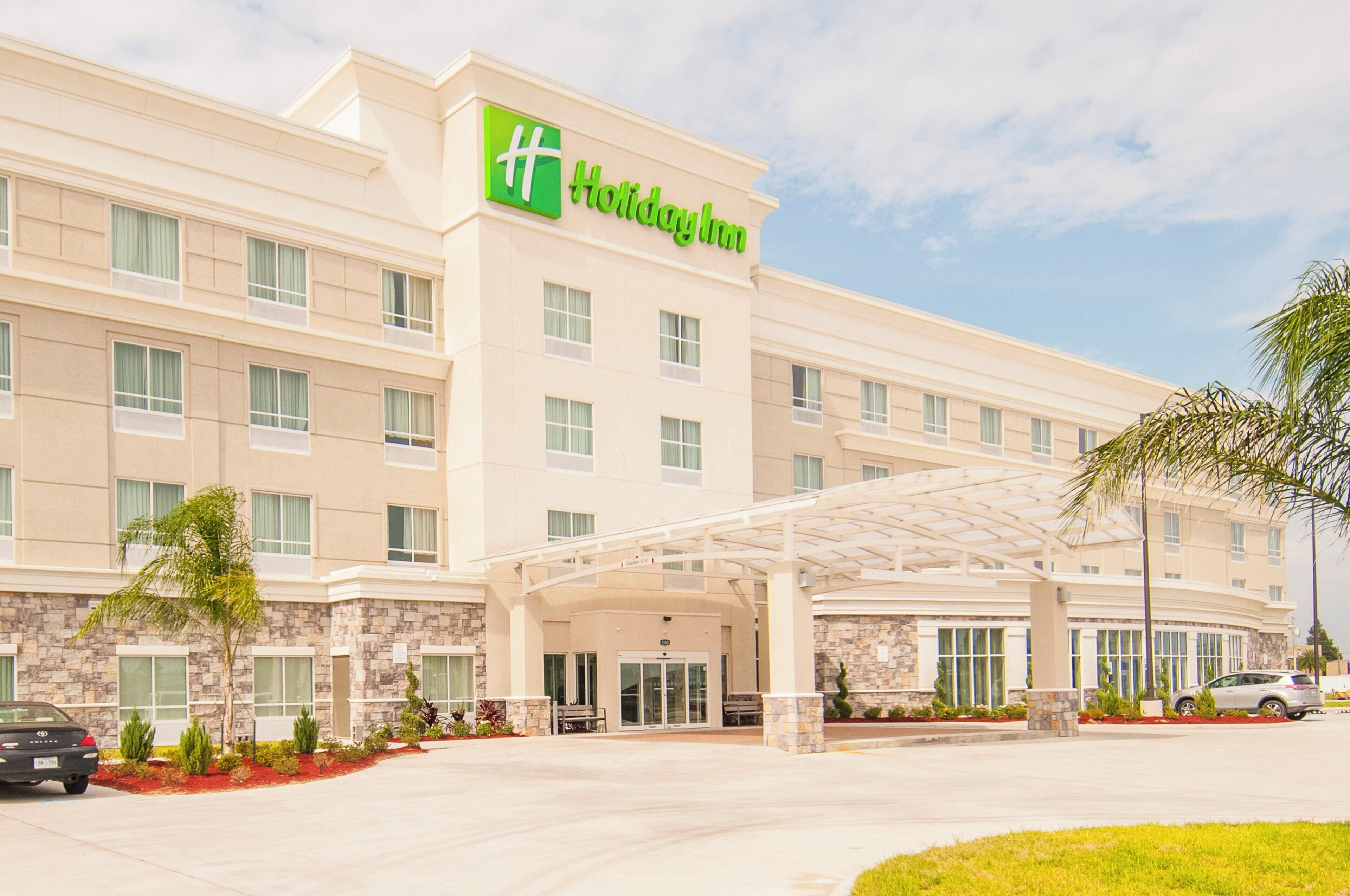 Un hotel con logotipo verde, varios pisos, entrada cubierta y zona de estacionamiento.
