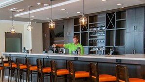 Un espace bar avec un barman, des tabourets de bar et un présentoir à bouteilles de vin.