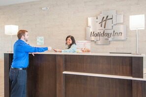 Mostrador de recepción en Holiday Inn con un cartel que indica el camino a la Sala de Reuniones y al Restaurante y Bar.