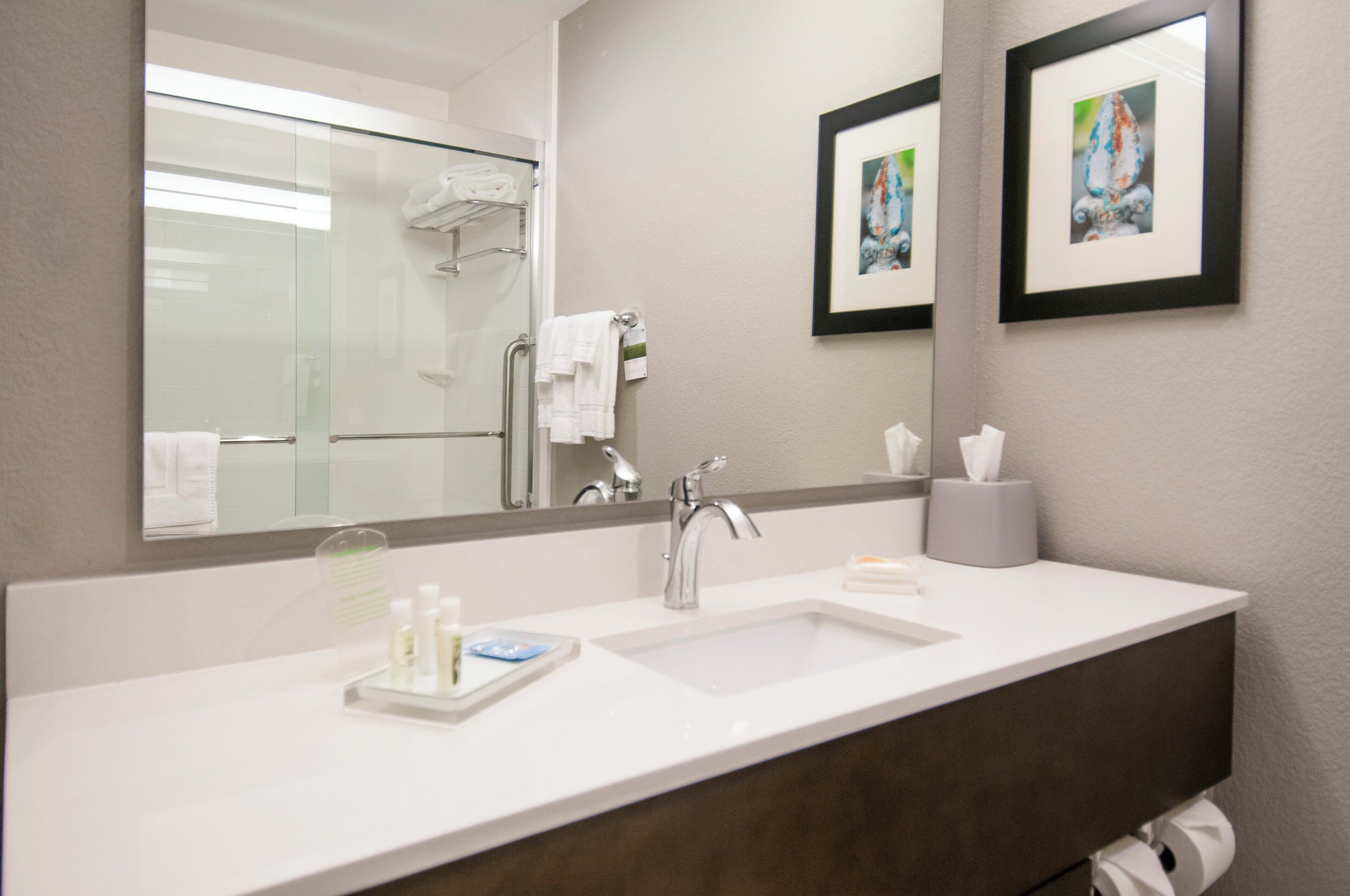 A hotel bathroom with a large mirror, two sinks, a towel rack, and framed artwork on the wall.