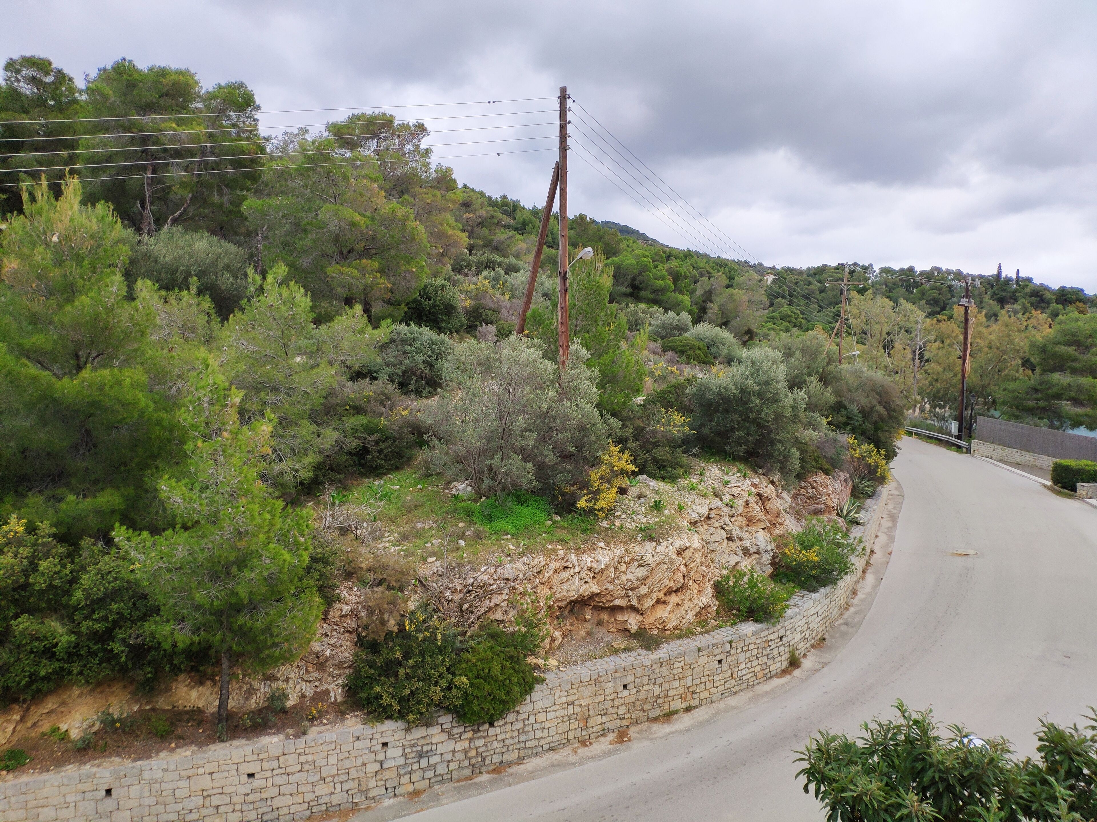 A rural road with a stone wall and vegetation on one side.