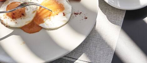 A breakfast setting with a plate of eggs, bacon, and greens, a glass of water, and a cup of coffee on a table.