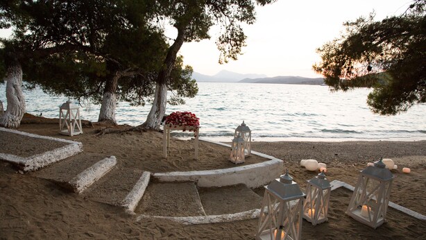 A beach setting with a wooden bench, lanterns, and a flower arrangement. - Xenia Poros Image Hotel (Poros)