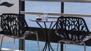 A balcony with two chairs and a table, overlooking a harbor with boats and a hillside town. - Xenia Poros Image Hotel (Poros)