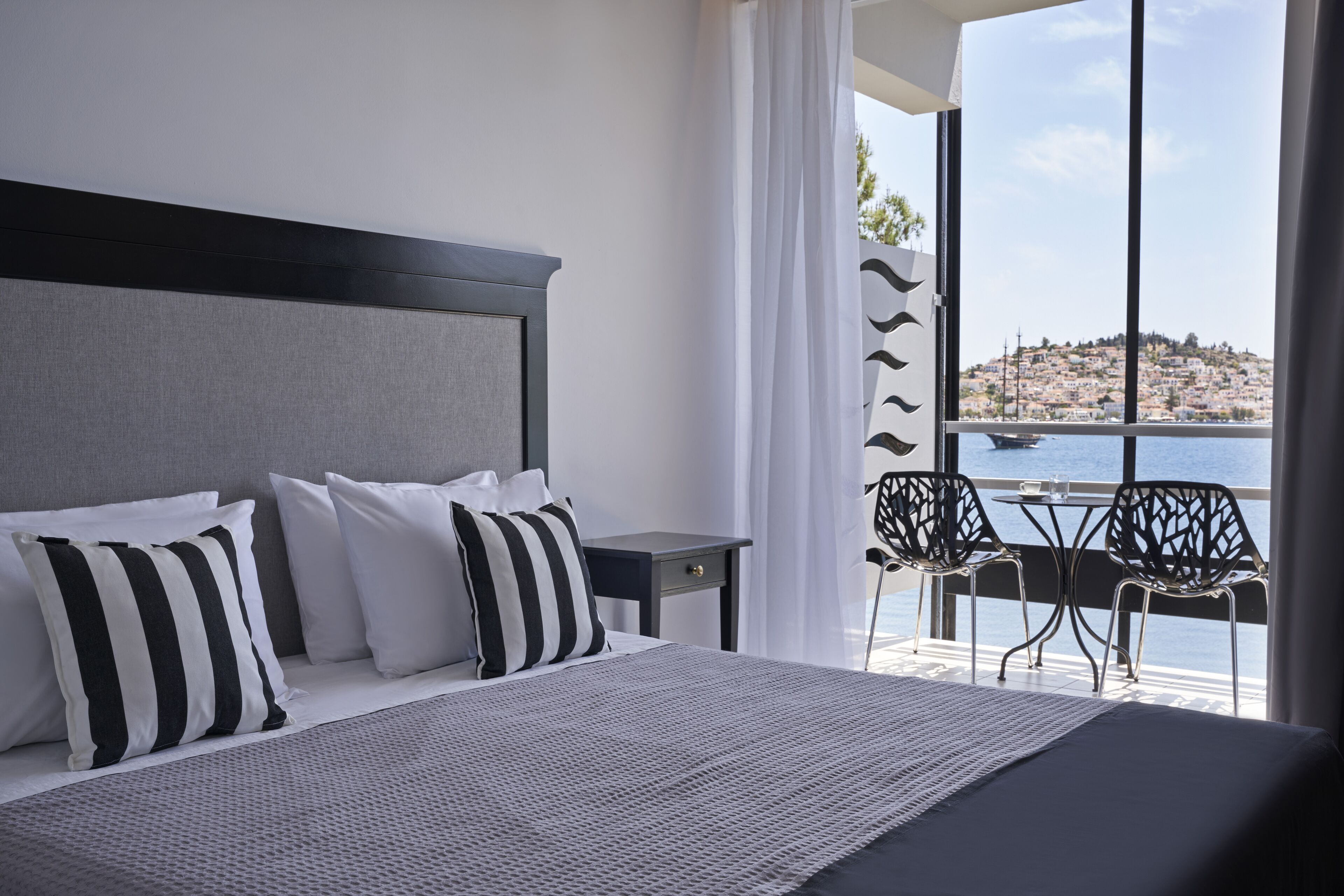 A modern bedroom with a large bed, a nightstand, and a view of a body of water and a hillside.