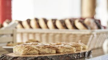 A wooden cutting board with pastry on it, a wicker basket of pastries in the background, and a red object to the left.
