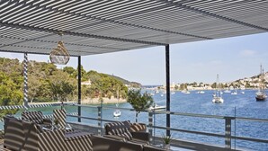 A covered outdoor seating area with wicker furniture and a view of the marina. - Xenia Poros Image Hotel (Poros)