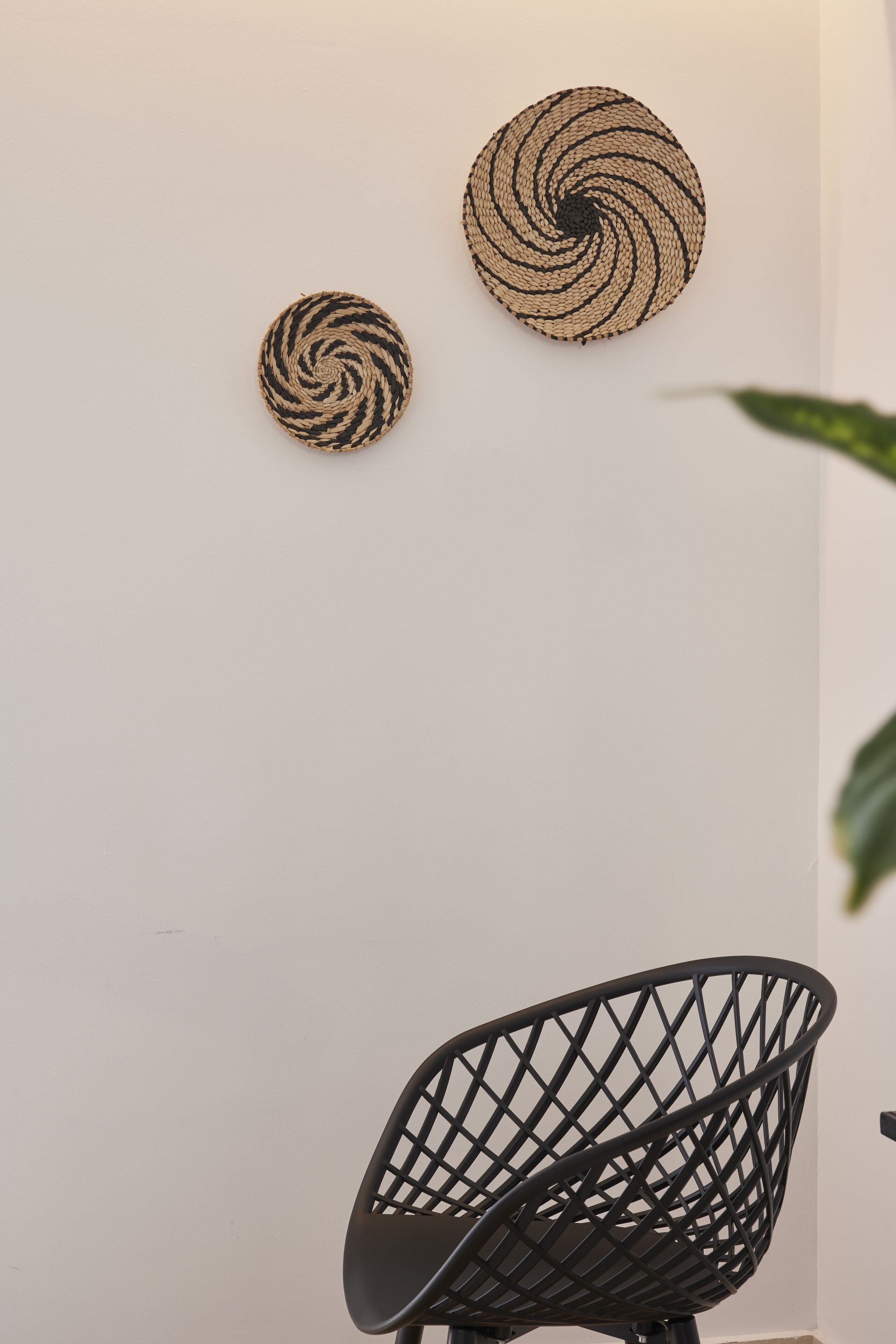 A wall with two woven wall hangings and a black wireframe chair.