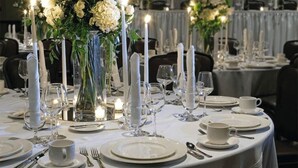 A table set for a formal dinner with white tablecloths, candles, and floral centerpieces.