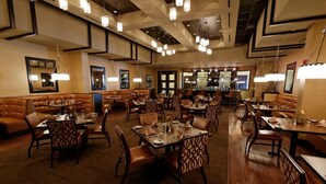 A restaurant with multiple dining areas, including booths and tables, with overhead lighting and a bar in the background.