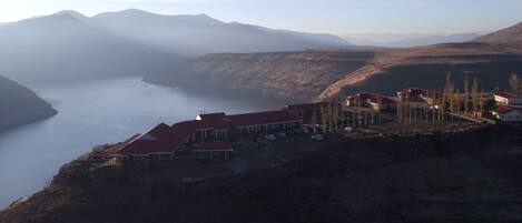 A mountainous landscape with a body of water, a cluster of buildings with red roofs, and a parking area.
