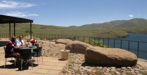An outdoor seating area with a table and chairs, overlooking a lake and hills. - Katse Lodge (Bokong)
