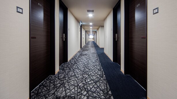 A hotel hallway with a patterned carpet, dark wooden doors, and a light-colored wall. - Daiwa Roynet Hotel Hakata - Gion (Fukuoka)