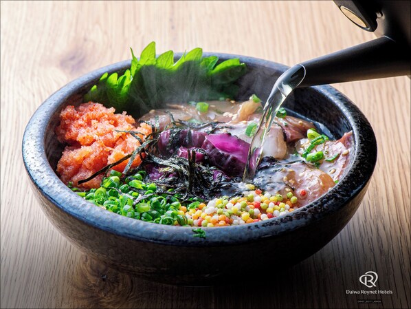 Un cuenco de hot pot con diversos ingredientes como verduras y mariscos, a donde se añade caldo con una cuchara grande.