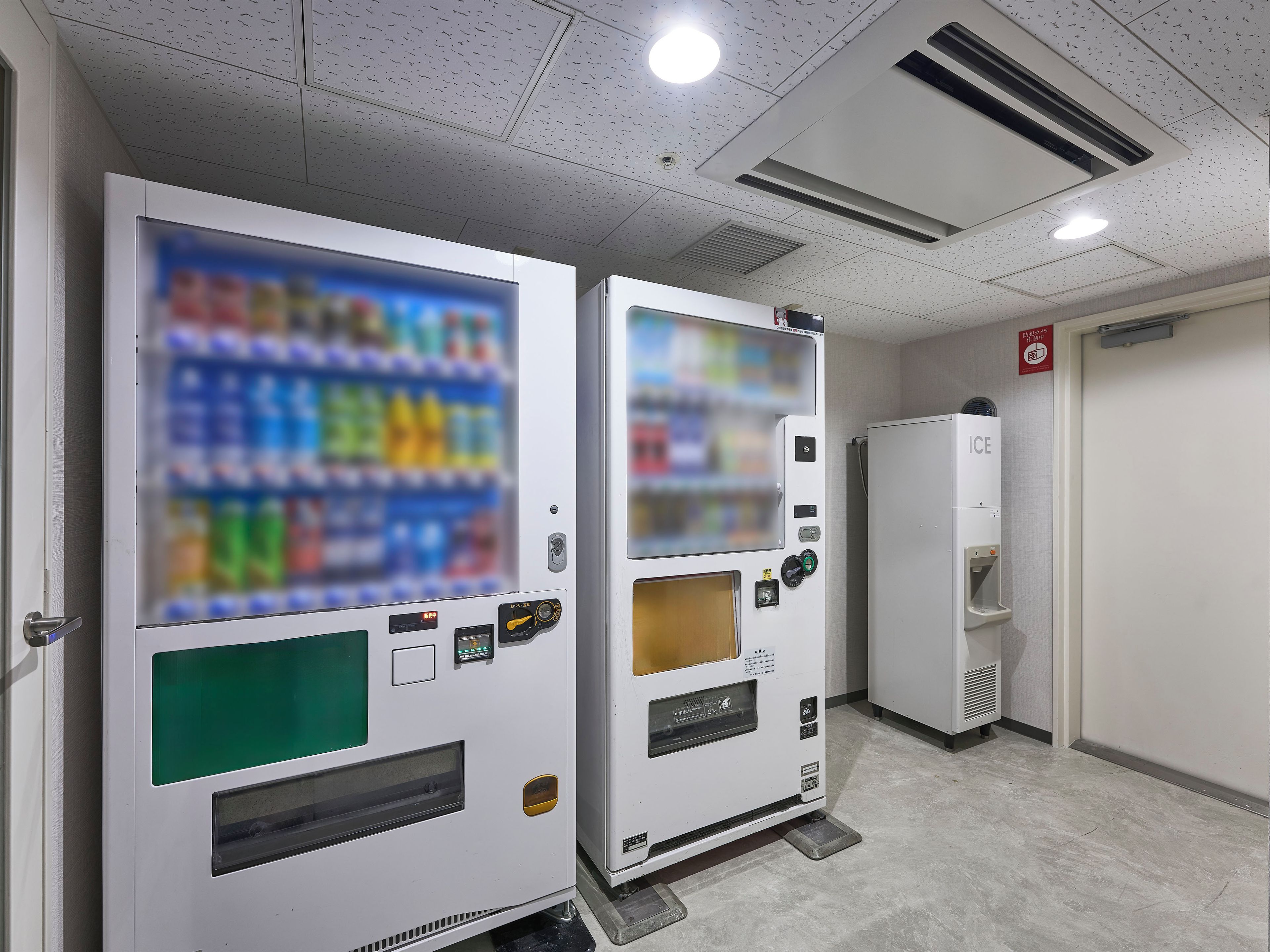 Vending machines with a selection of beverages and a refrigerator in a hallway.