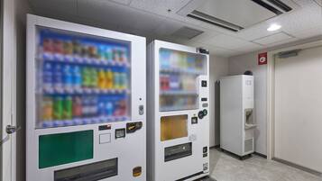 Vending machines with a selection of beverages and a refrigerator in a hallway.