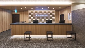 Una recepción de hotel con mostrador de registro, dos sillas y un letrero en la pared.