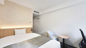 Una habitación de hotel moderna con una cama grande, una mesita de noche, una silla y una pequeña mesa.