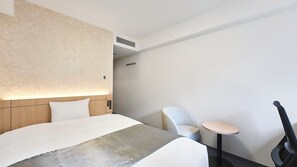 Una habitación de hotel moderna con una cama grande, una mesita de noche, una silla y una pequeña mesa.