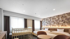 Habitación de hotel con una cuna, un escritorio, una cama y zona de estar.