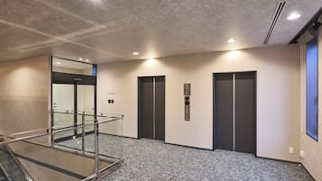A modern elevator area with a glass railing, a carpeted floor, and a wall-mounted elevator control panel.