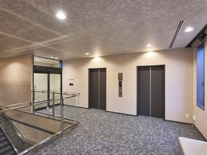 Un área de ascensor moderna con barandilla de vidrio, suelo alfombrado y panel de control de ascensor en la pared.