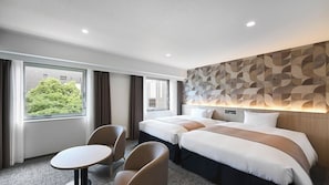 Habitación de hotel con dos camas, una mesa de comedor y vistas a un edificio y árboles.