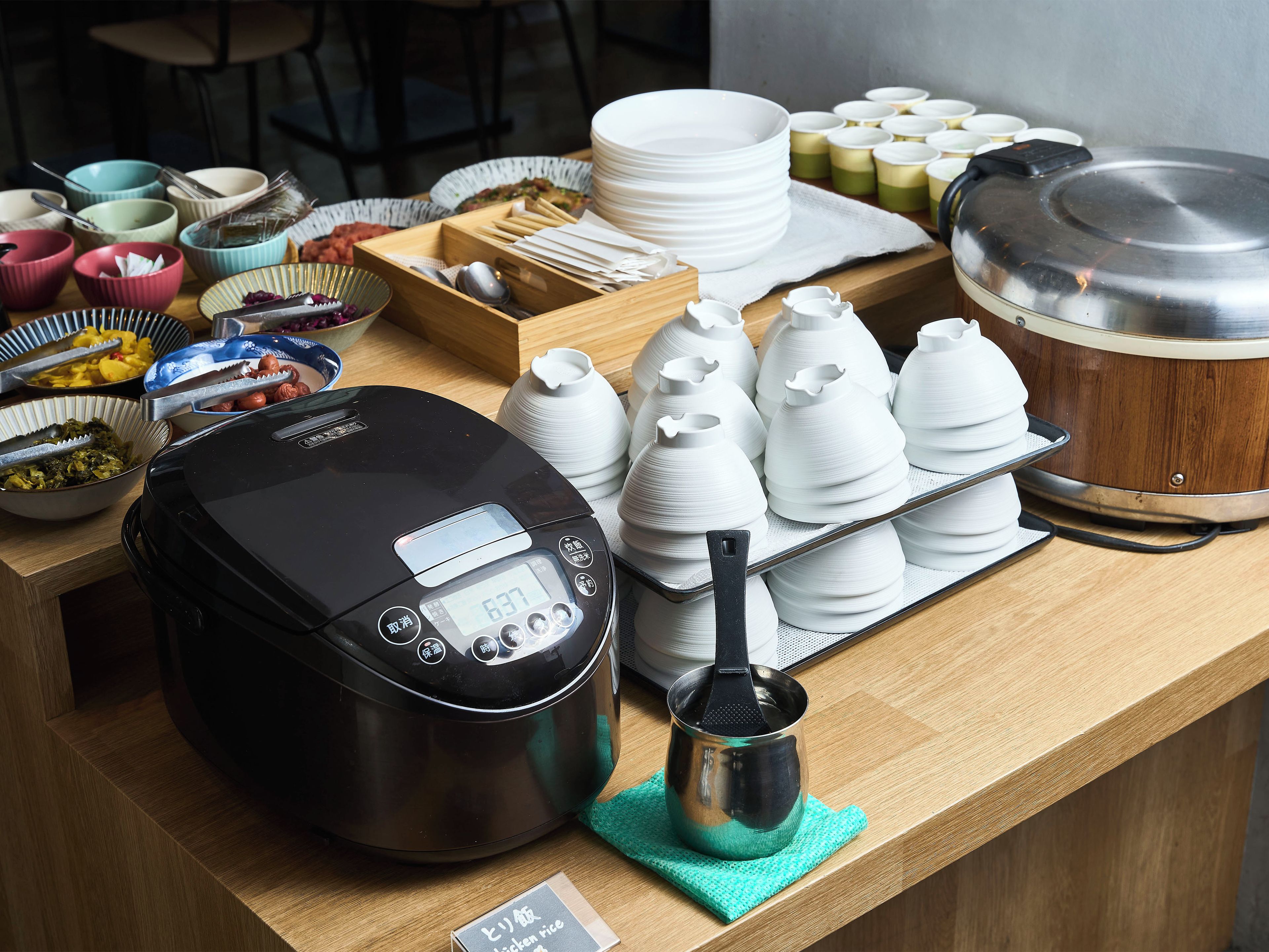 Un piano di lavoro in cucina con una cuociriso, ciotole, piatti e teiere.