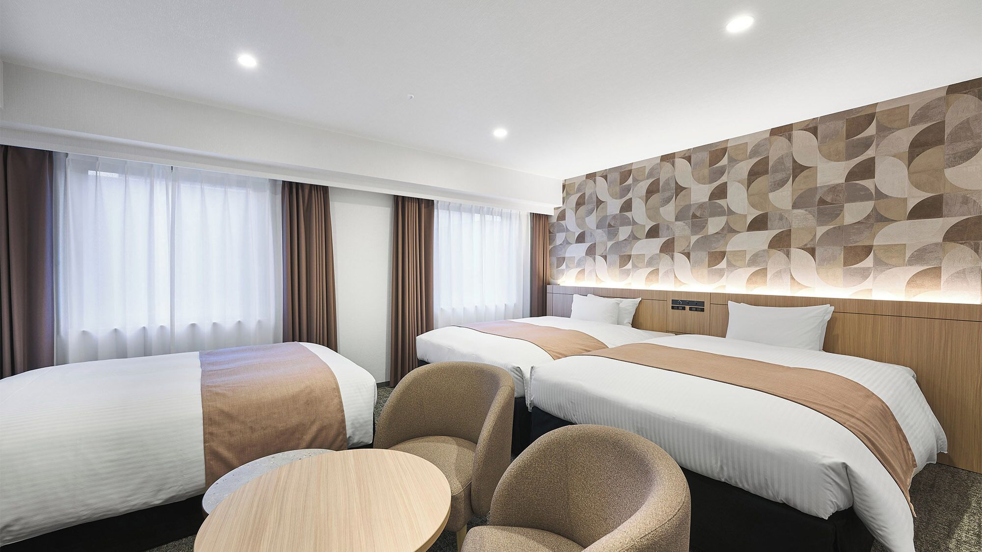 Hotellihuone, jossa on kaksi sänkyä, oleskelualue ja koristeellinen seinä.