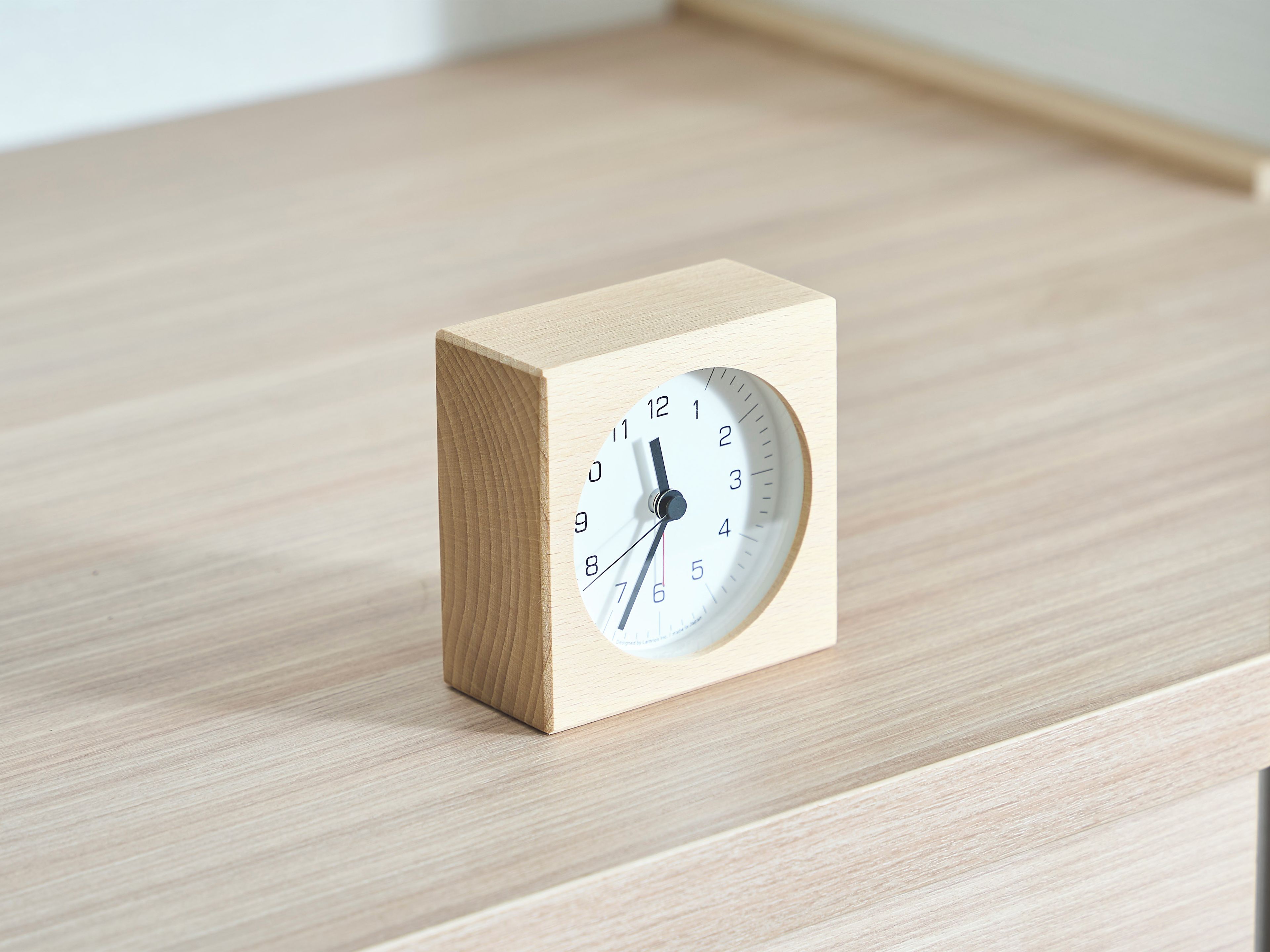 A wooden cube-shaped clock with a white face and black numerals on a wooden surface.