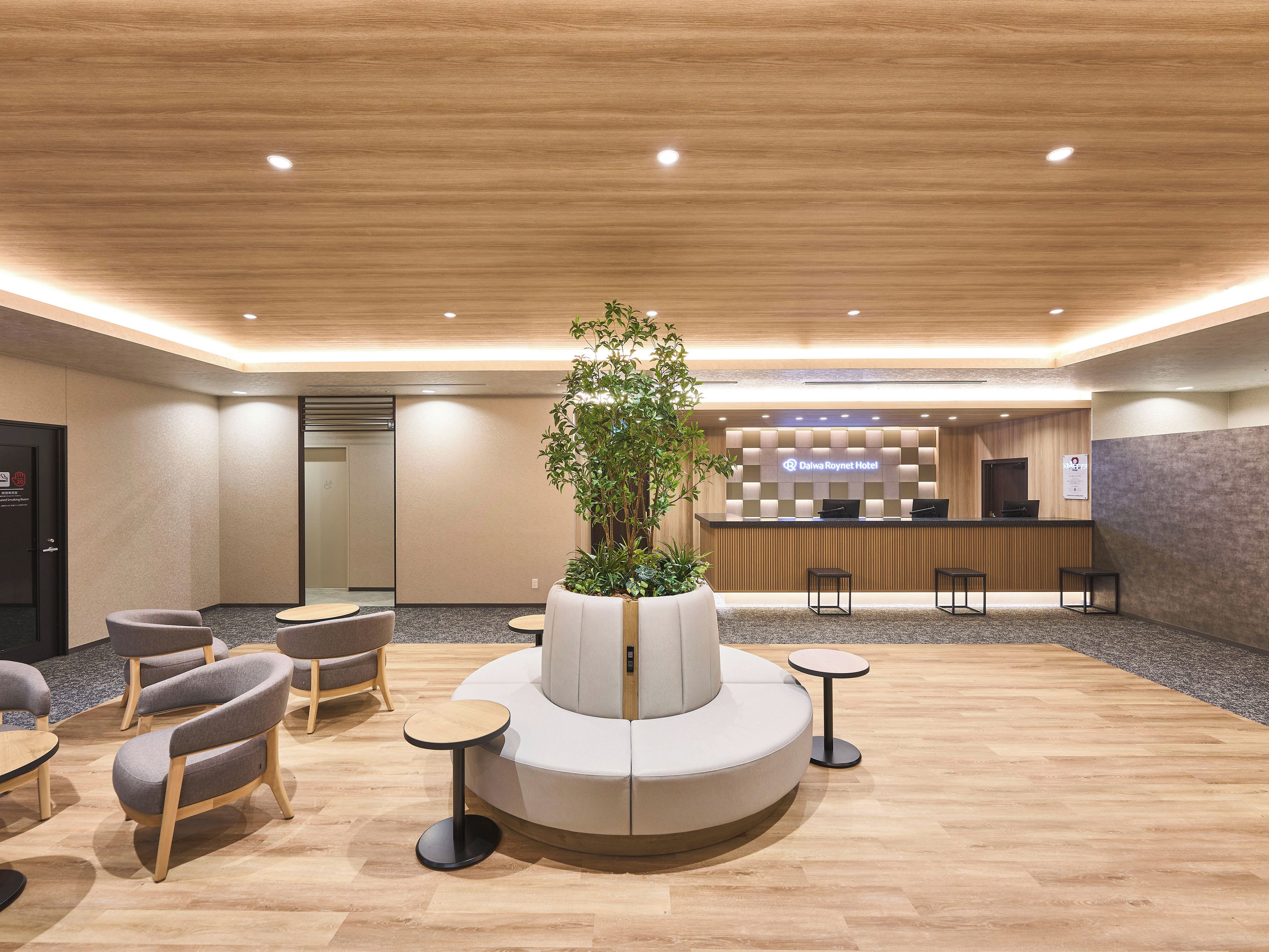 A hotel reception area with a modern design, featuring a reception desk, seating arrangements, and a central plant.