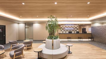 A hotel reception area with a modern design, featuring a reception desk, seating arrangements, and a central plant.
