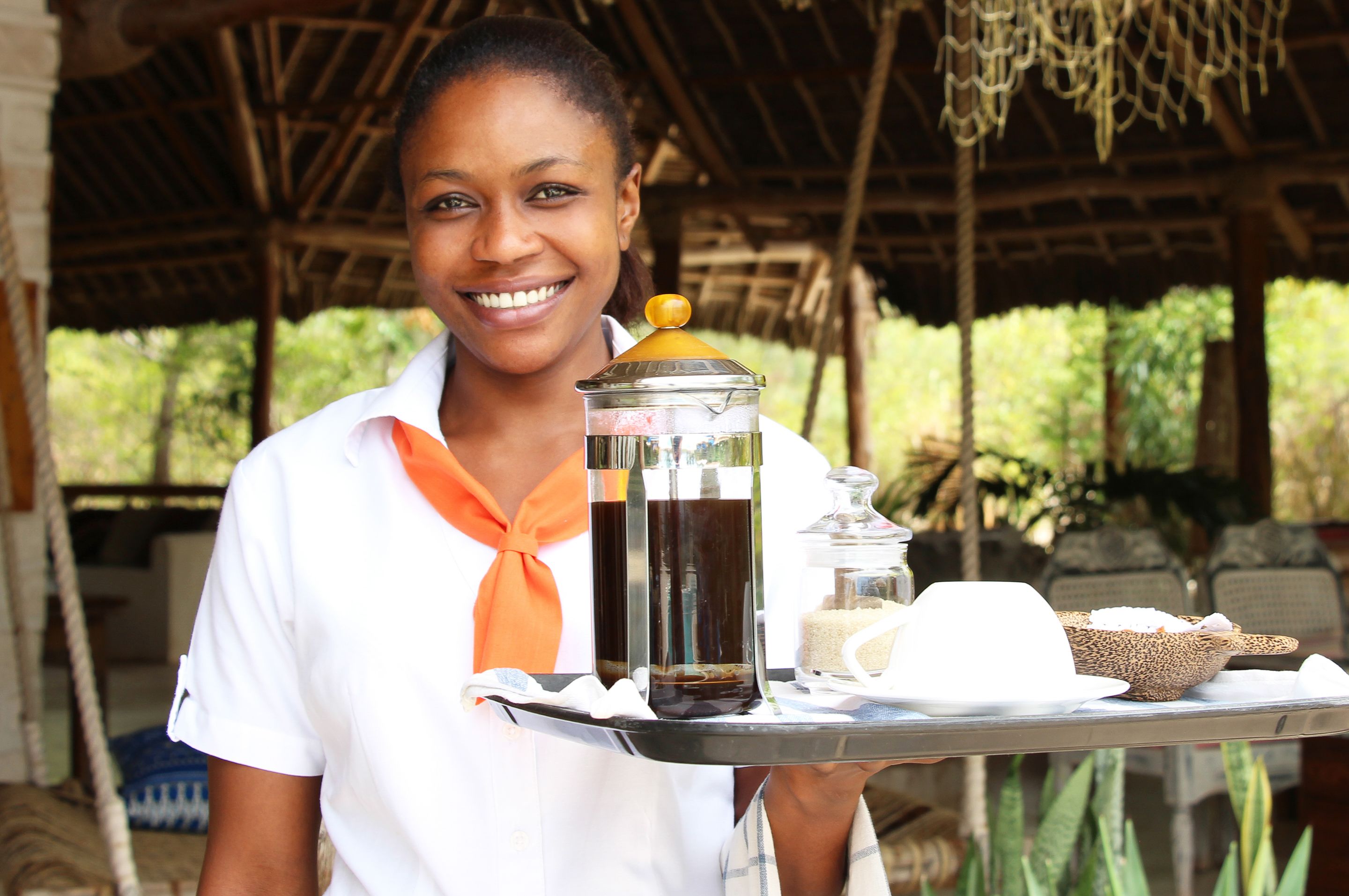A person holding a tray with a beverage container, a glass, and a basket of bread.
