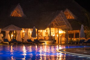 A poolside area with thatched-roof structures, lounge chairs, and umbrellas. - The Charming Lonno Lodge (Watamu)