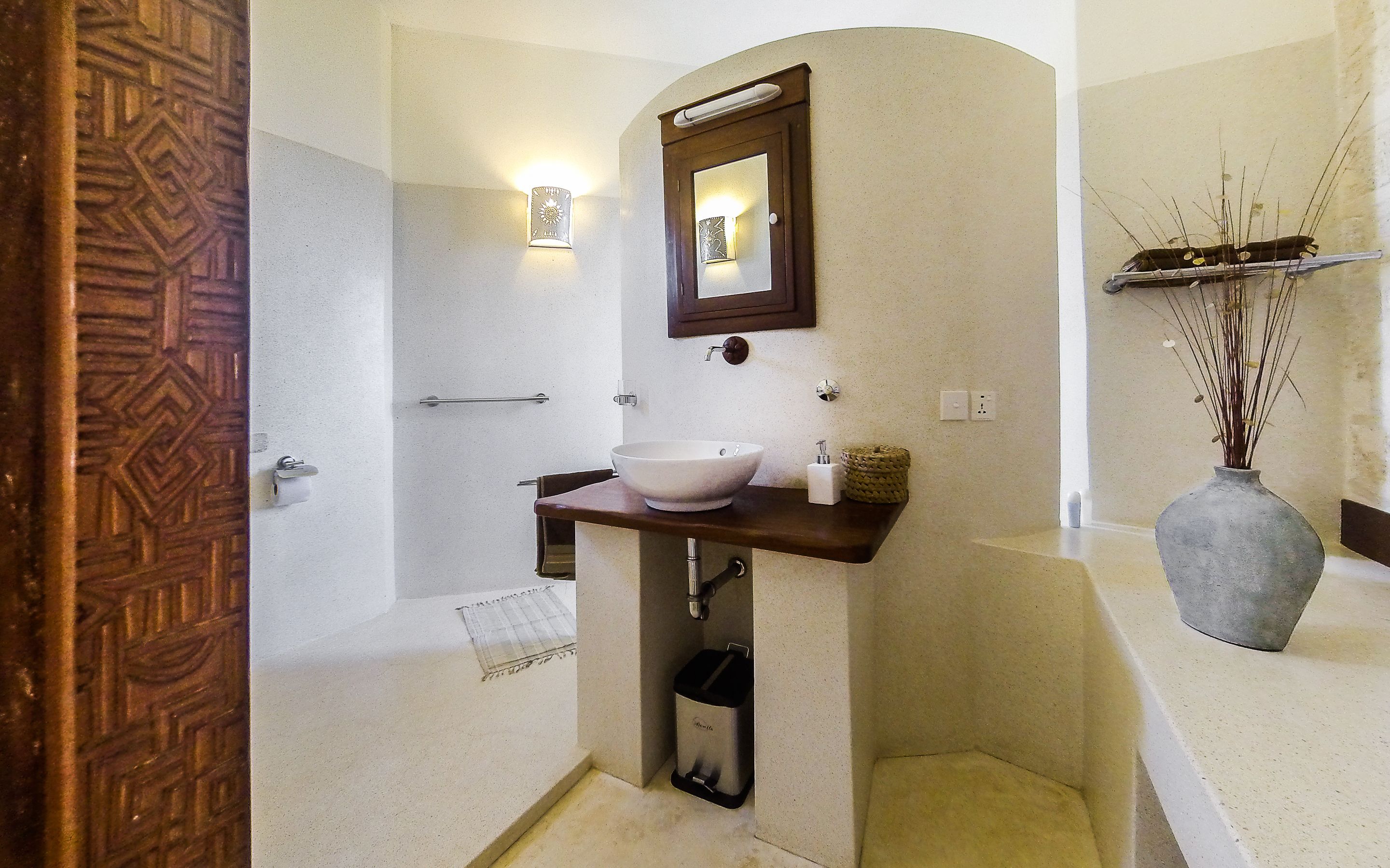 A bathroom with a freestanding sink, a mirror, a towel rack, a trash bin, and a shower area.