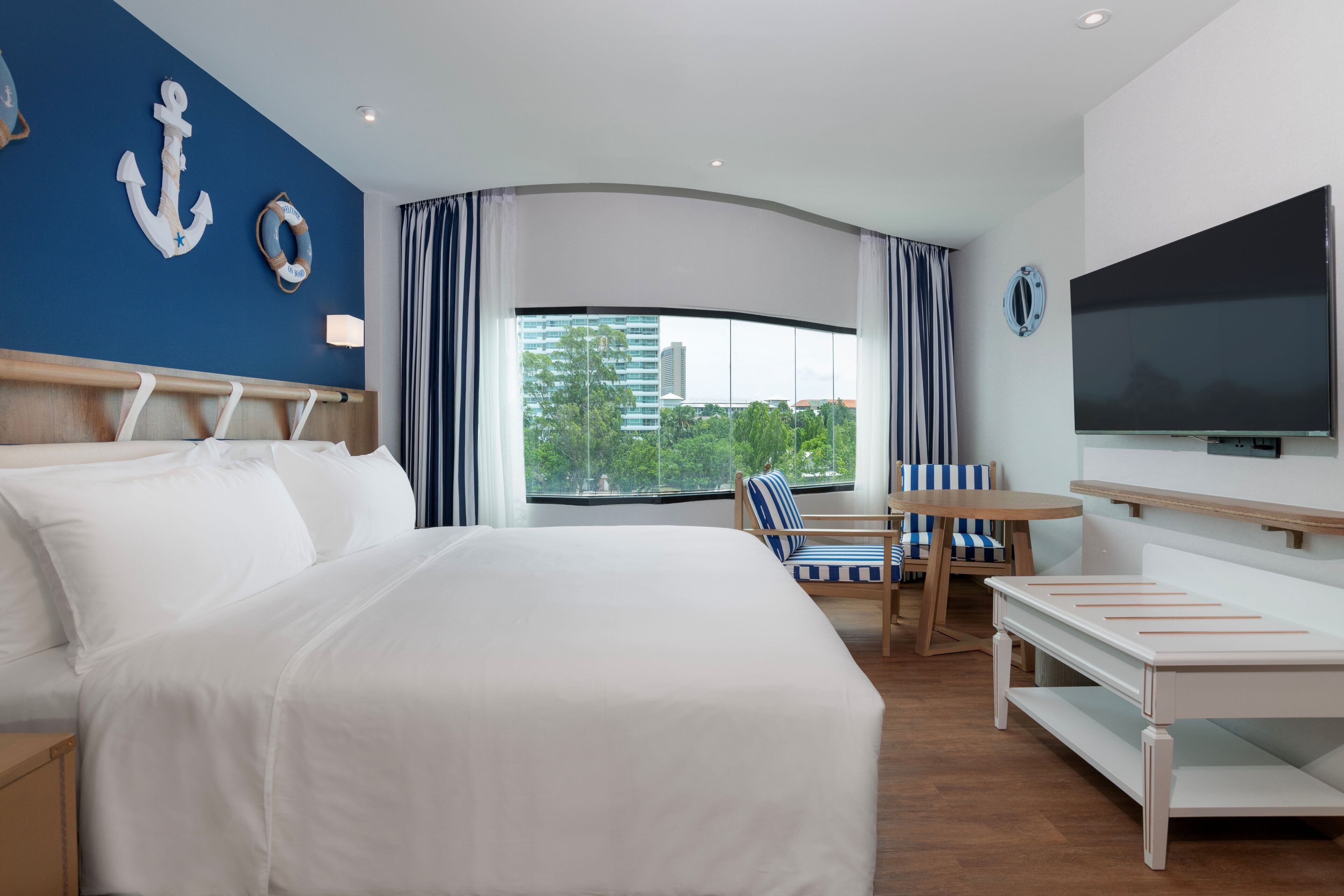 A hotel room with a large bed, a TV, a desk, and a view of the city.