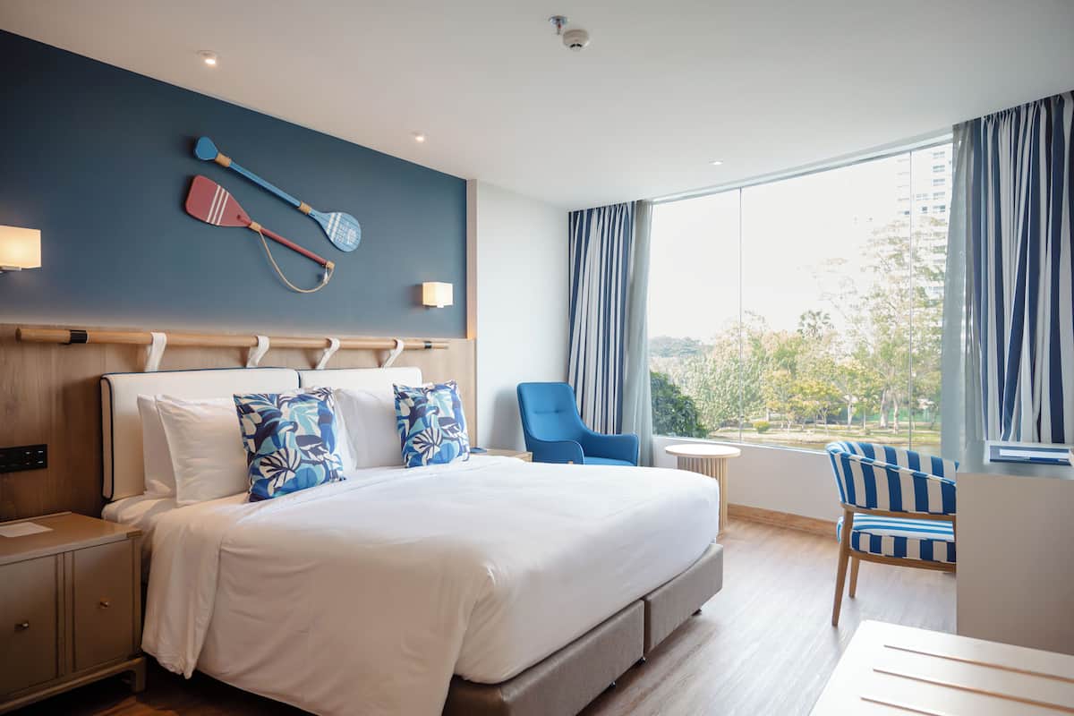 Een hotelkamer met een groot bed, een stoel, een bureau en uitzicht op de omgeving.