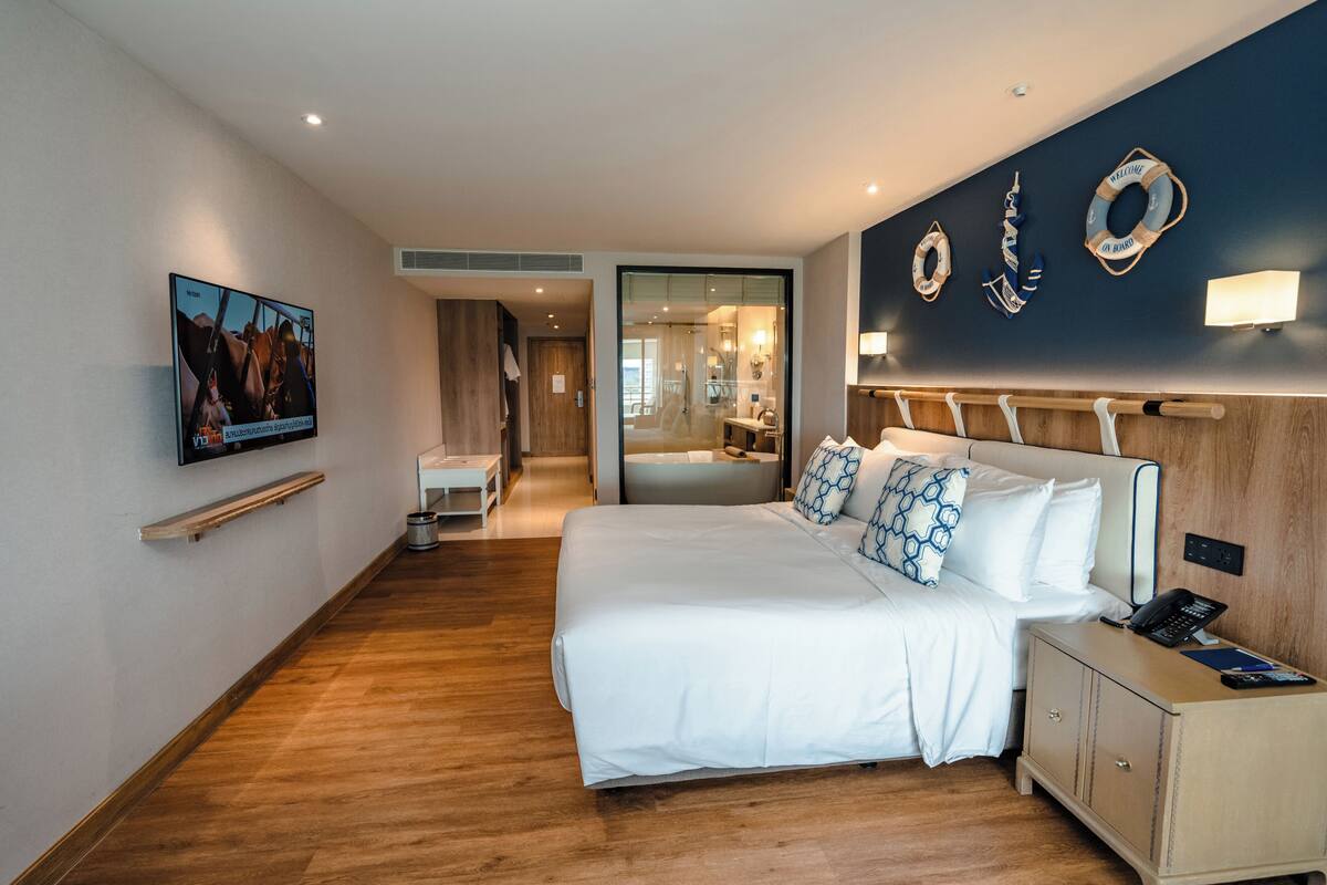 Een hotelkamer met een groot bed, nachtkastje en een aan de muur bevestigde televisie.