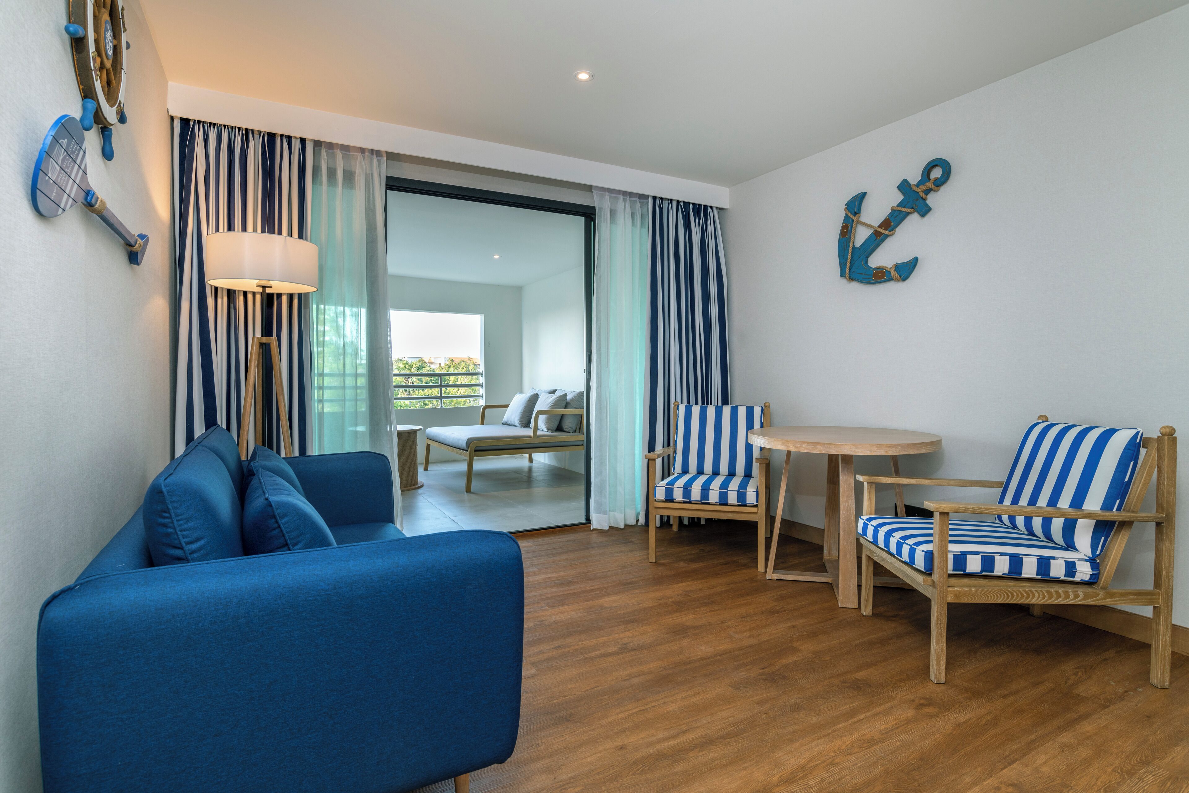 A modern room with a blue sofa, striped armchairs, a small round table, and a view to an outdoor balcony.