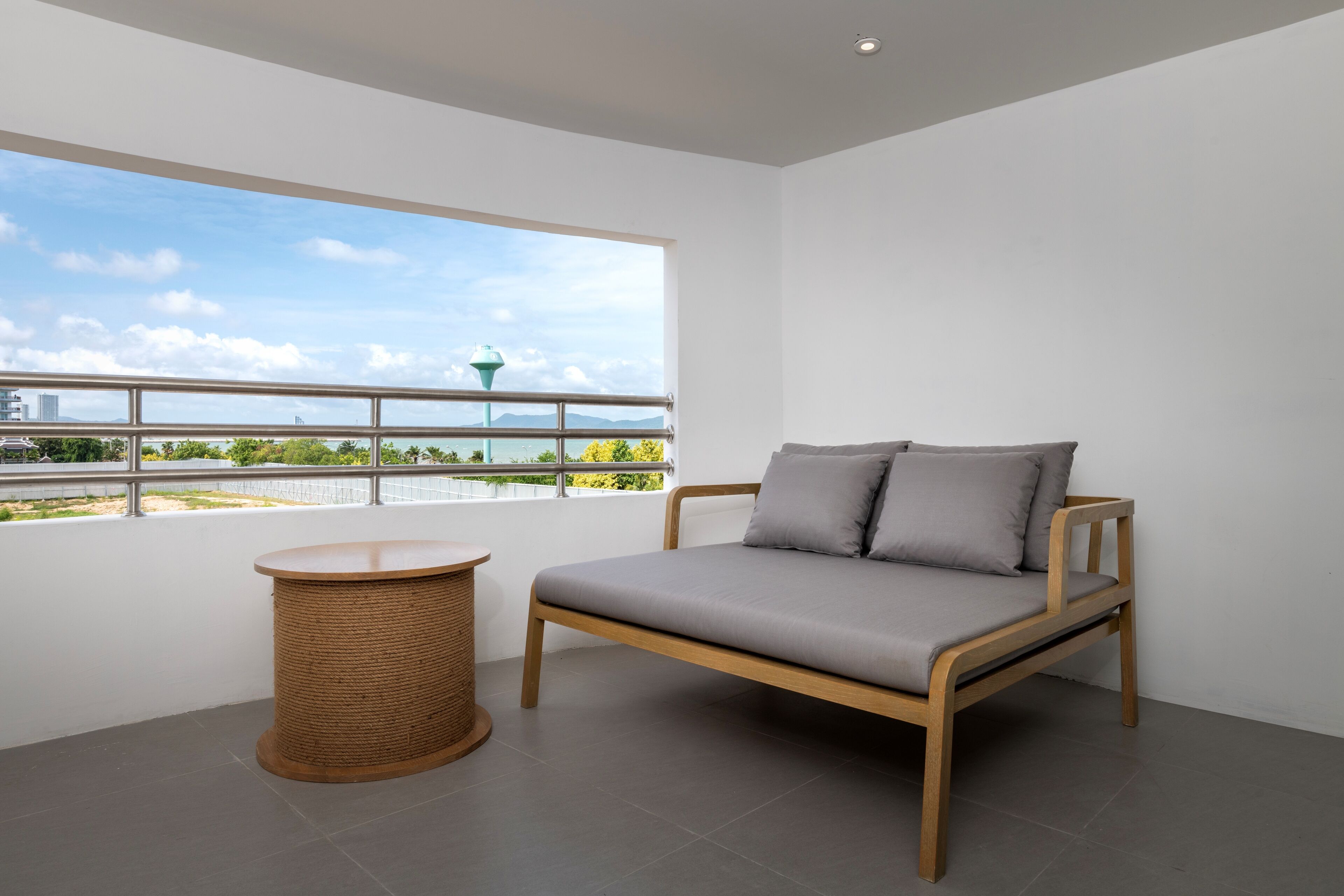 A modern room with a wooden bed, a round wicker side table, and a large window offering a view of a cityscape and greenery.