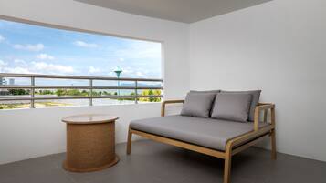 A modern room with a wooden bed, a round wicker side table, and a large window offering a view of a cityscape and greenery.
