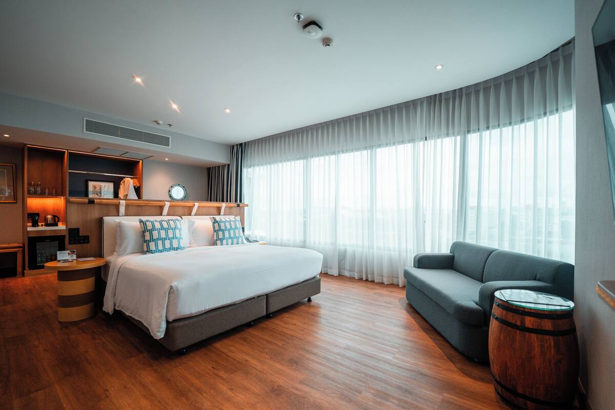 Een moderne hotelkamer met een groot bed, een bank, een houten vat en een groot raam met dunne gordijnen.