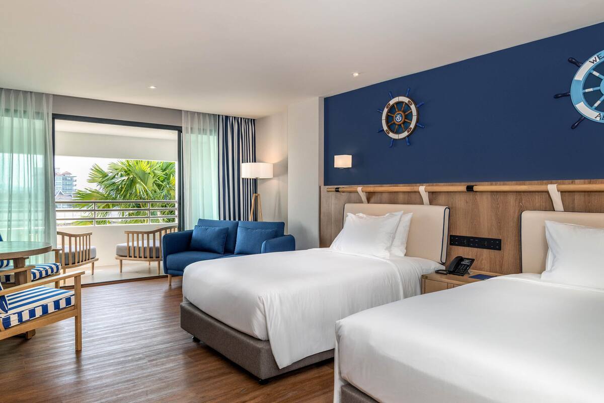 Een hotelkamer met twee bedden, een bank, een stoel, een lamp en uitzicht op de omgeving.