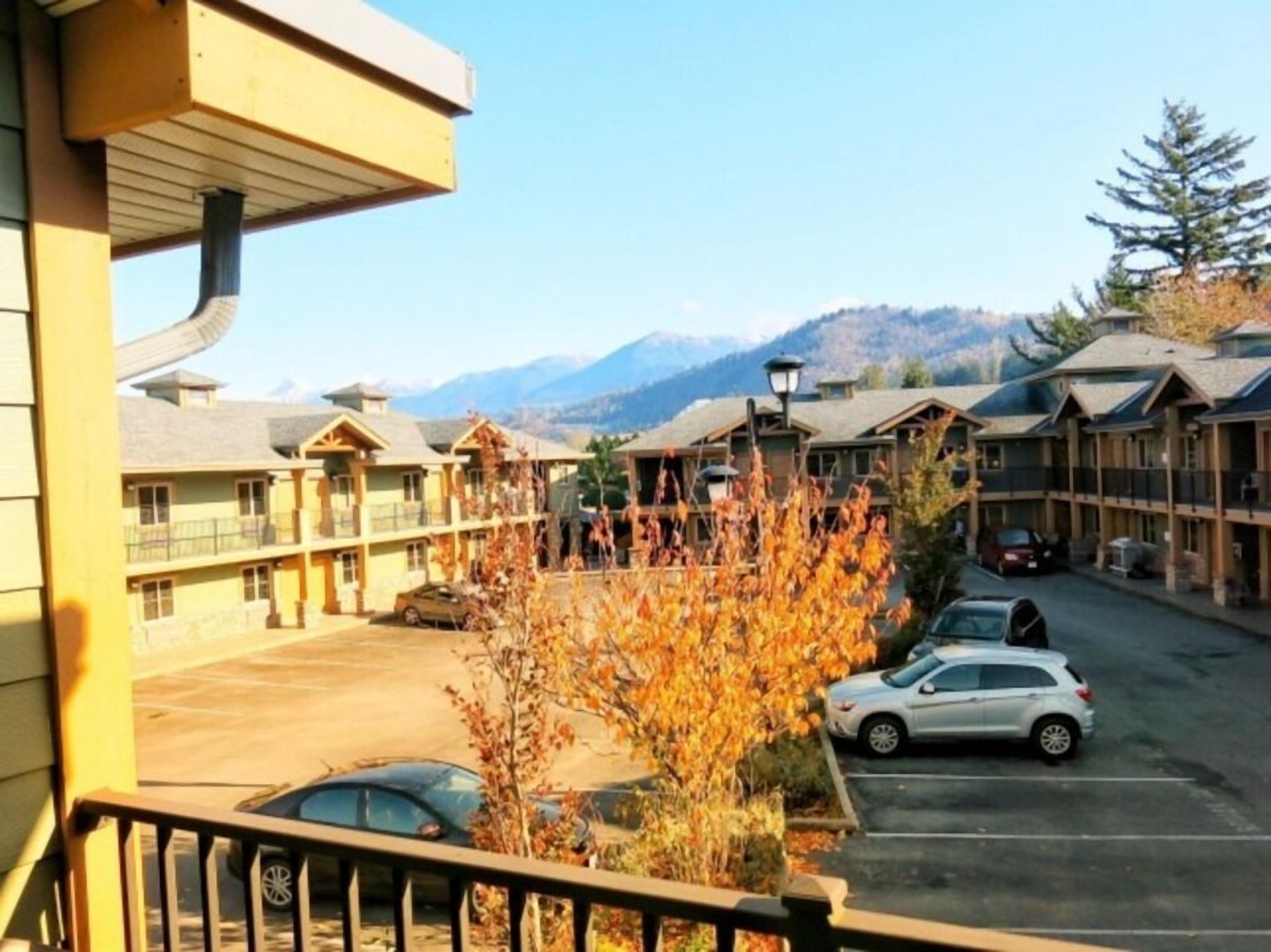 A hotel with multiple-story buildings, a parking area, and a mountain backdrop.