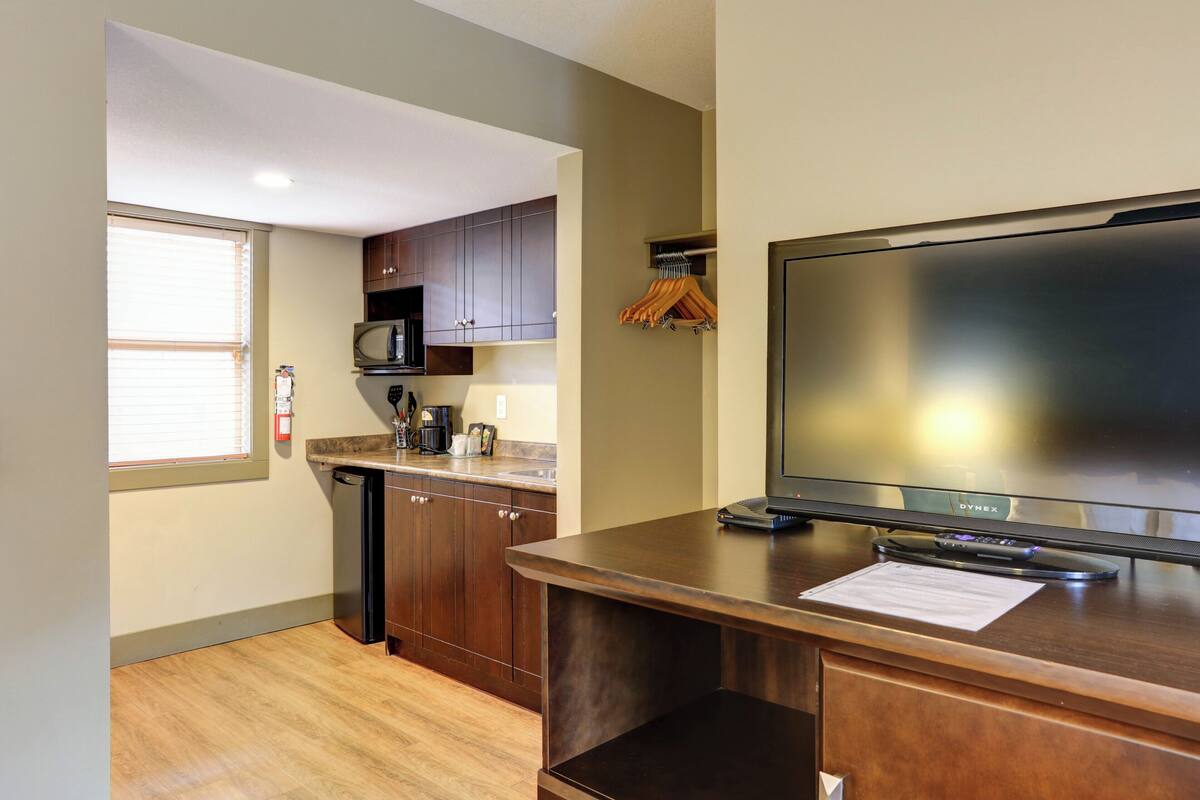 A kitchen with wooden cabinets, a microwave, and a flat-screen TV on a wooden counter.