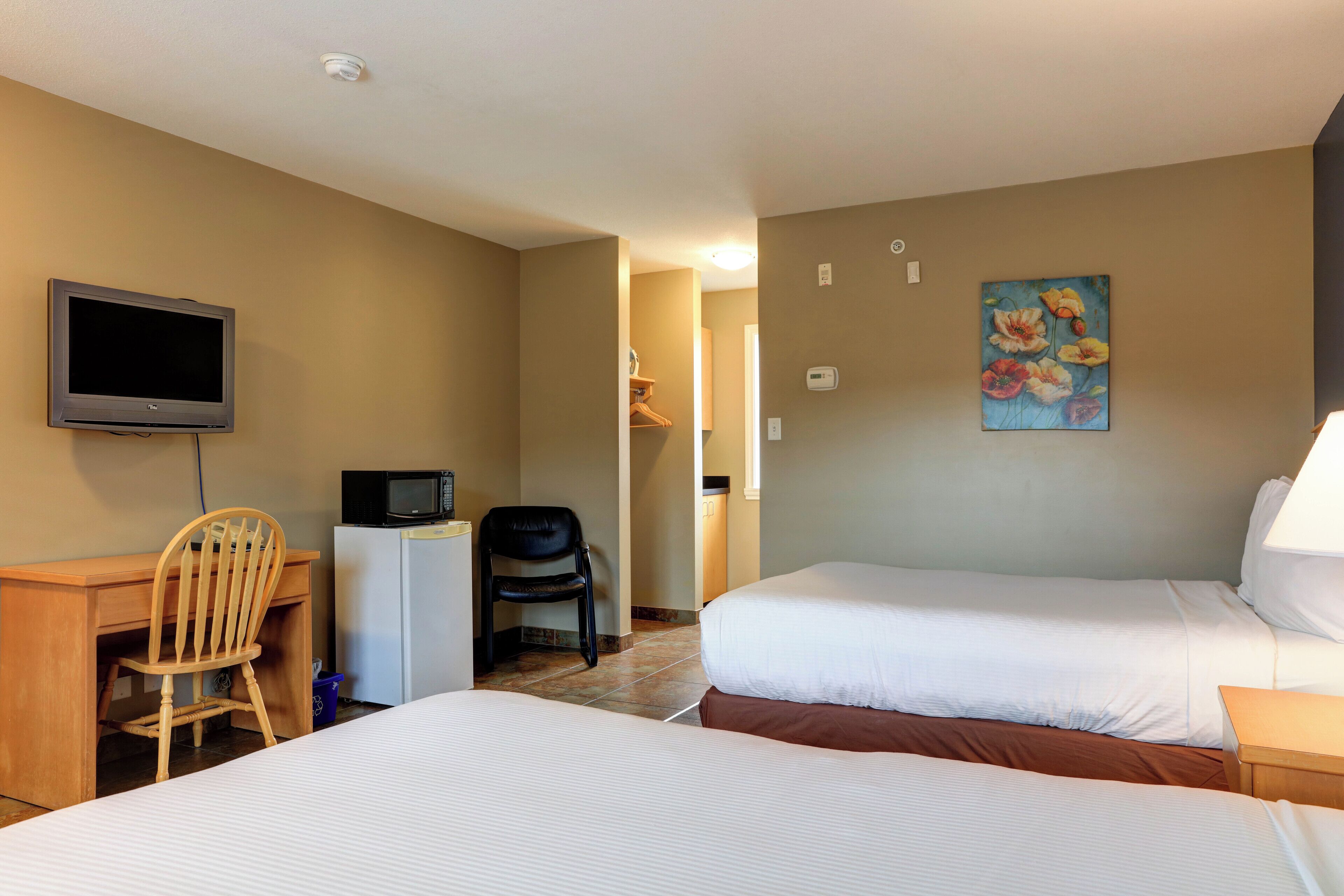 Ein Hotelzimmer mit zwei Betten, einem Schreibtisch mit Stuhl, einem Fernseher und einer Mikrowelle.