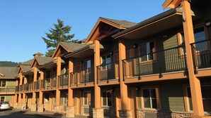 A row of multi-story buildings with balconies, stone pillars, and a clear blue sky.