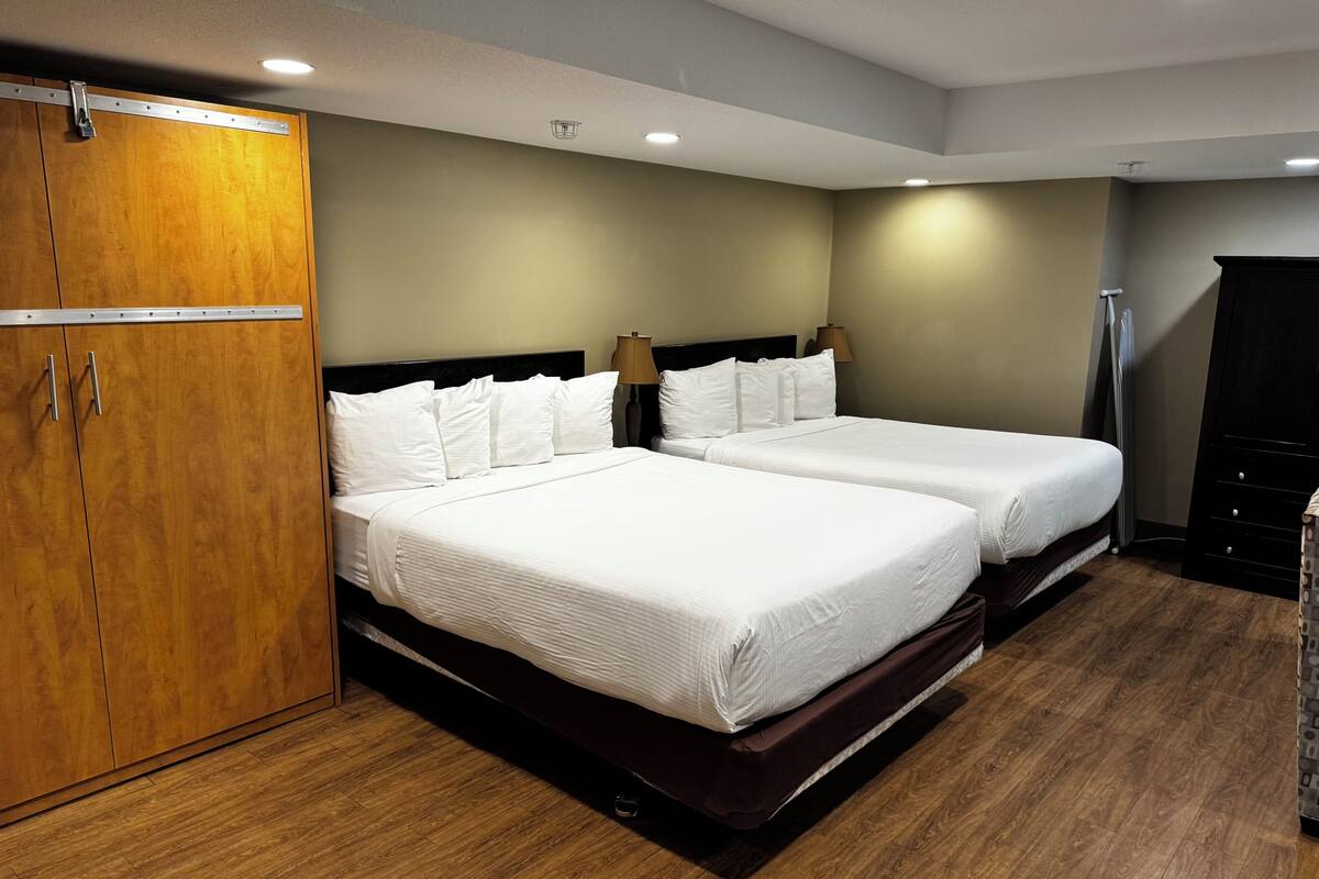A hotel room with two beds, wooden wardrobe, and a lamp.