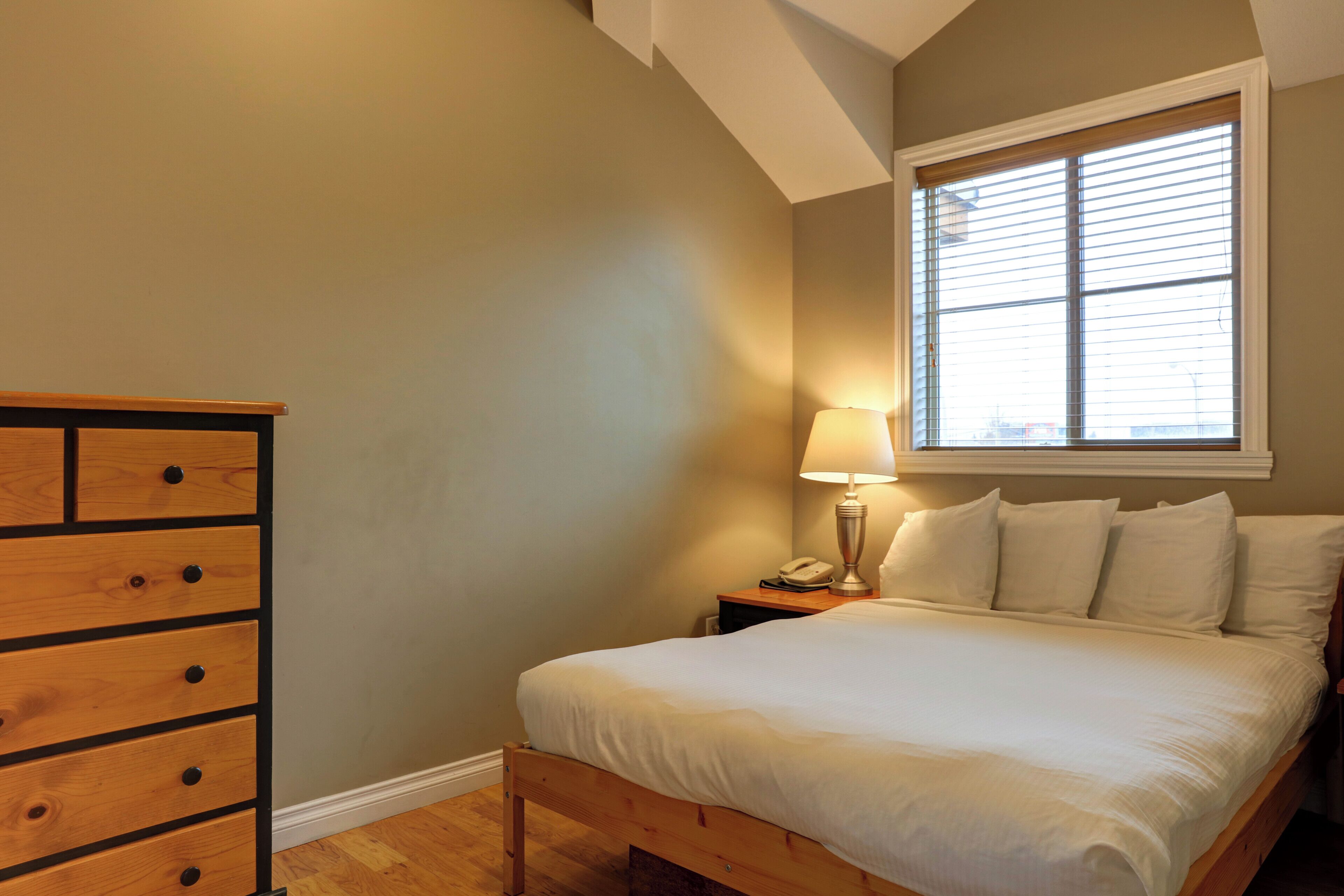 A bedroom with a wooden bed, a nightstand with a lamp, and a dresser.